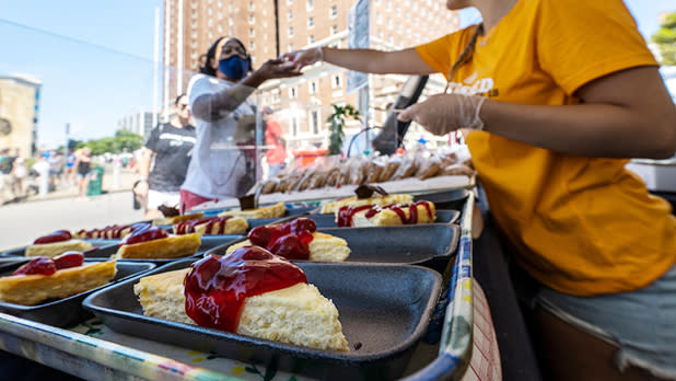 A woman in an orange shirt hands a customer a slice of cheesecake topped with cherries at Taste of Buffalo