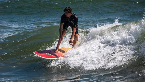 A person on an orange surfboard rides a wave in Montauk