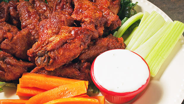 Crispy, saucey Buffalo wings on a plate with celery, carrot sticks, and red cup of blue cheese dip