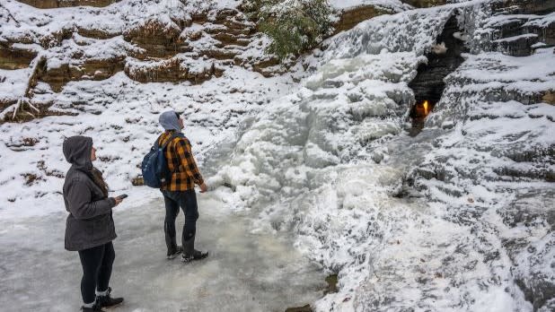 Snowshoeing- Adirondacks near Saranac Lake - Photo by NYS ESD Two people gaze up at a small flame nestled behind a frozen waterfall