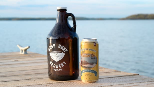 A growler and beer can from Wood Boat Brewery in Clayton, NY sitting on a dock by the river.