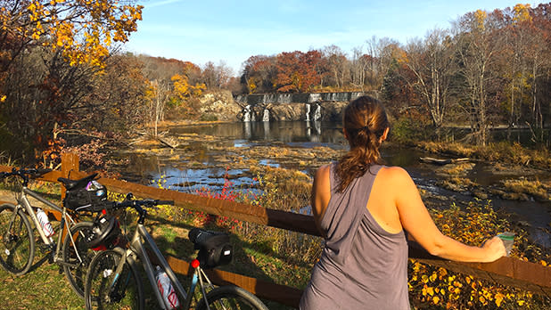 A woman takes a break from biking the Empire State Trail to look at the rushing water of Stuyvesant Falls