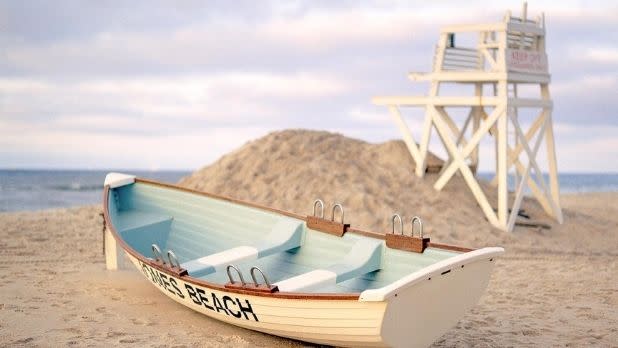 A white lifeguard chair and cream colored row boat sitting on the white sand beach in Jones Beach State Park on Long Island