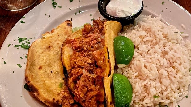 Tacos with shredded meat on a plate with white rice, limes, and sour cream