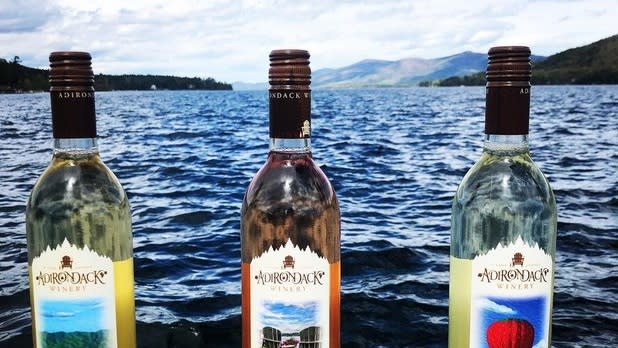 Three bottles of Adirondack Winery wine sit in front of dark blue lake waters