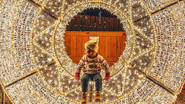 A boy in winter clothing sitting in a verticle circle of white and yellow fairy lights