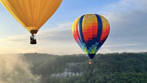 Two hot air balloons soar through the blue skies over the green forests at Letchworth