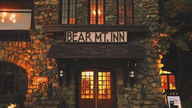 View of the front of a stone building illuminated by warm light with signage that reads "Bear Mt. Inn"