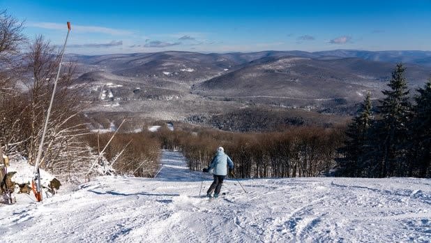 A skier races down a snowy slope with the Catskill Mountains in the background