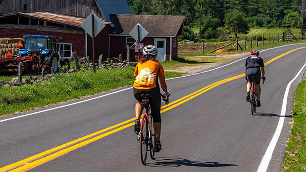 Two people riding bikes pass by a barn in Jay in the Adirondacks