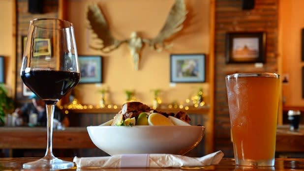 A glass of wine, pine of beer, and a lunch dish on a table at Bitters & Bones
