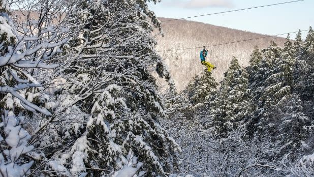 A person ziplines among snow-covered trees