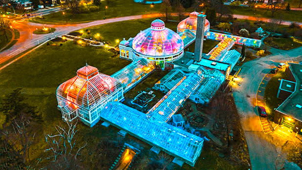An aerial view of the Buffalo and Erie County Botanical Gardens building and glowing multi-colored festival lights seen through the glass dome rooftops