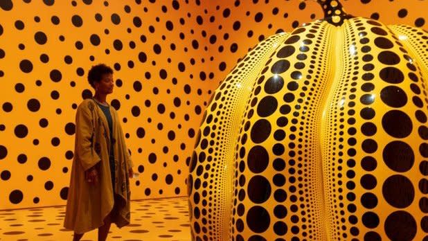 A woman stands in an orange and black spotted Infinity Room by Yayoi Kusama
