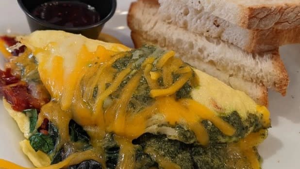 An omelette with Sun-dried tomatoes, basil pesto, spinach, and cheddar-jack cheese next to a stack of toast from Dina's in Ellicottville