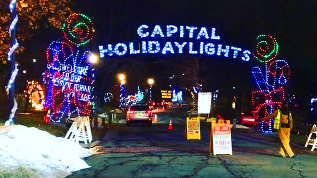 The drive-thru entrance with a glowing blue neon sign and multi-colored light displays of popsicles and candy canes surrounding each side of the Capital Holiday Lights sign