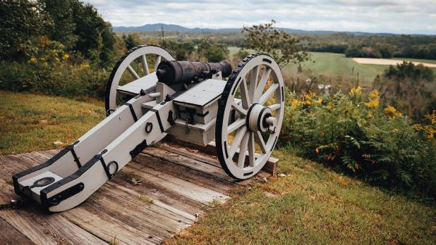 a replica Revolutionary war cannon points out at a sprawling field