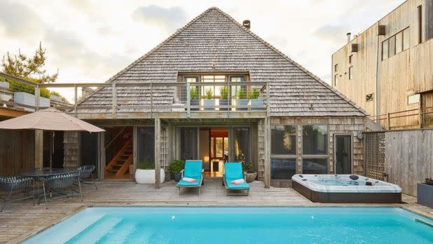 Pyramid shaped Airbnb in front of an in-ground pool, with patio furniture and a hot tub