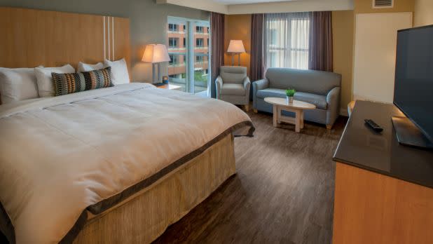 Comfortable hotel room with a large bed, soft lighting, and modern decor. A couch and armchair are near the window, creating a cozy, inviting atmosphere.