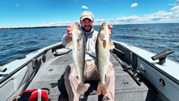 Man holding two fish while on a small boat