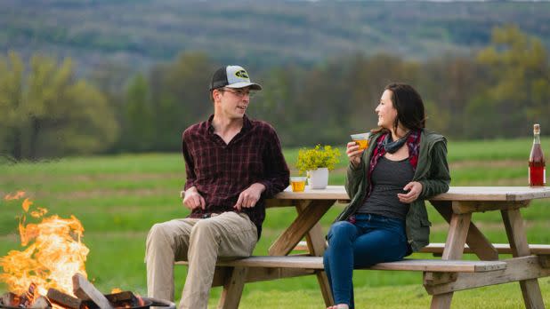 Two people sitting at picnic table holding ciders