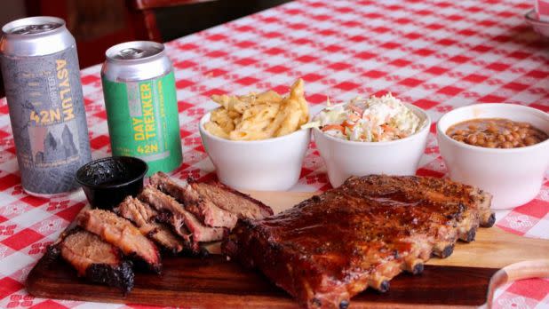 Craft beer cans next to a BBQ meal on a picnic table