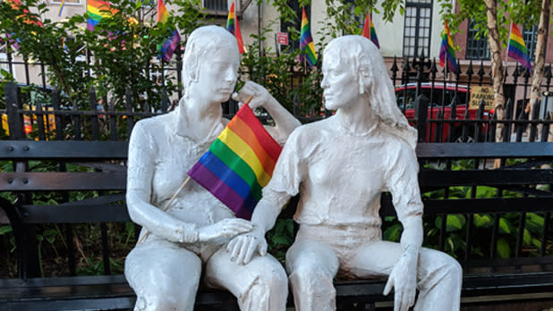 Statues of two people in Christopher Park holding a rainbow flag