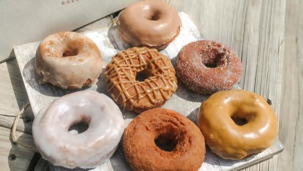 A plate of seven donuts decorated with different glazes, sugars, and drizzles