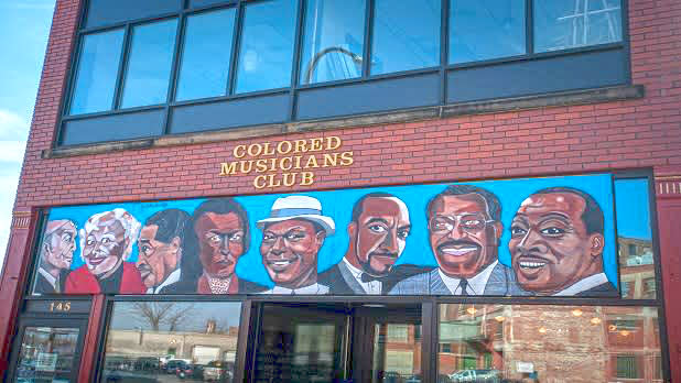 Mural of a row of 7 men and 1 woman on the brick exterior of the Colored Musicians Club in Buffalo.