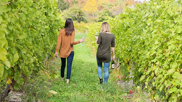 Two people walking through a leafy vineyard drinking wine in the Finger Lakes