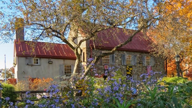 Purple flowers and a tree in front of the exterior of the Old Stone House