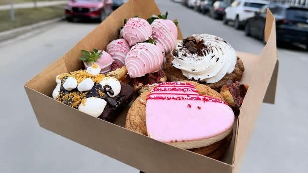 A box of pink chocolate-covered strawberries, pink heart-shaped cookies, and a cookie with white frosting.