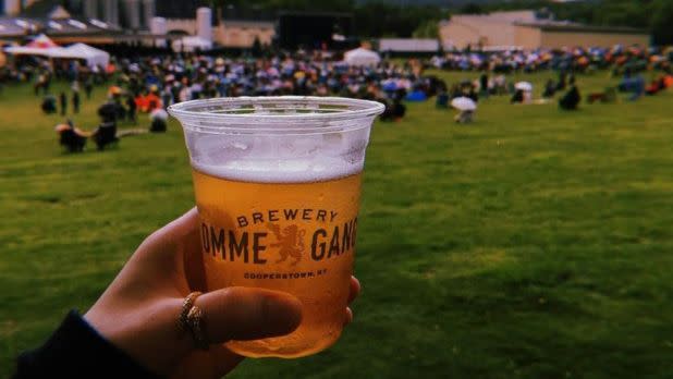 Person holding up beer in a cup that says "Brewery Ommegang"