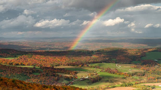 A rainbow bisects a valley filled with the bright oranges, yellows, and reds of fall