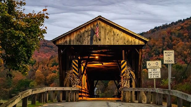The wooden Downsville Covered Bridge stretches across the East Branch of the Delaware River with colorful tree-covered hilltops sprouting up in the background