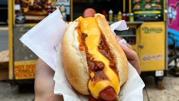 A hot dog topped with mustard in front of a Nathan's cart