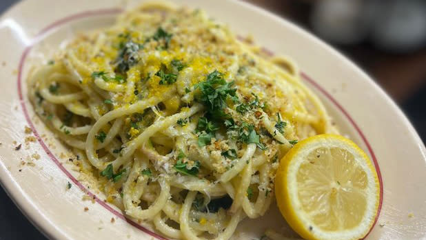 A plate of spaghetti with yellow sauce topped with green cilantro and a slice of lemon