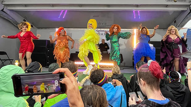 A group of drag queens dressed in the colors of the Pride flag perform on stage at Rochester Pride