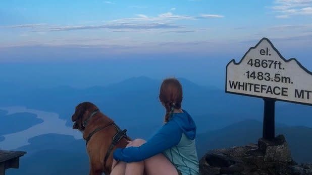 A girl and a dog sit at the top of Whiteface Mountain