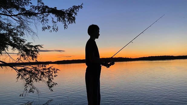 A silhouette of a boy fishing at sunset