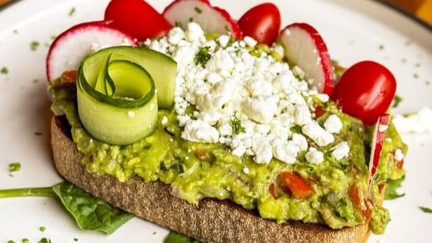 Avocado toast topped with radishes, tomatoes, cucumbers, and cheese