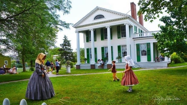 Children dressed in historical clothing play in front of the Genesee Country Village & Museum