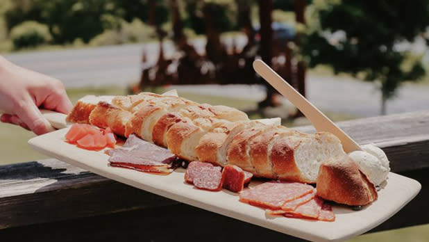 A plate of bread, cheese, and meats with a backdrop of a vineyard