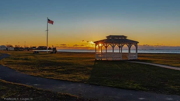 A pavilion and American flag in front of the beach and sunset at Shorefront Park