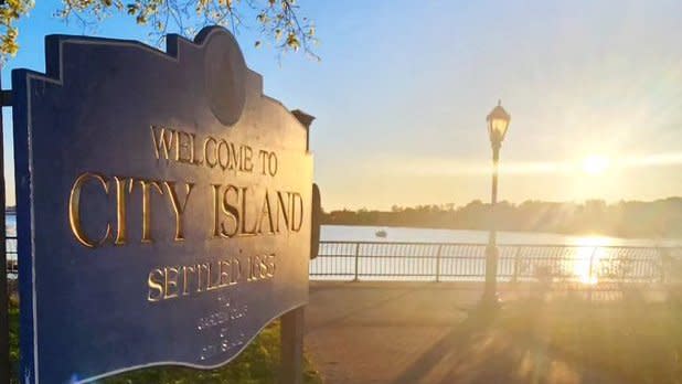 "Welcome to City Island" sign with sunset over the water in the background