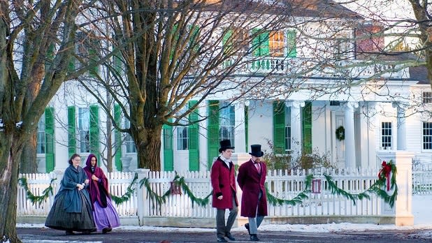 People in period dress stroll the snow-blanketed streets during Yuletide In The Country Tours at Genesee Country Village & Museum