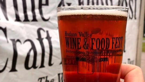 A person holding a pint of beer in a glass that reads "Hudson Valley Wine & Food Fest"