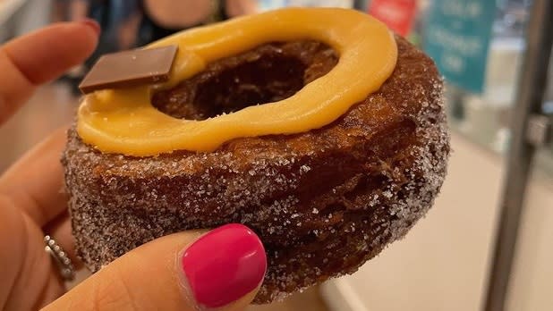 A brown cronut topped with caramel sauce and a slice of chocolate