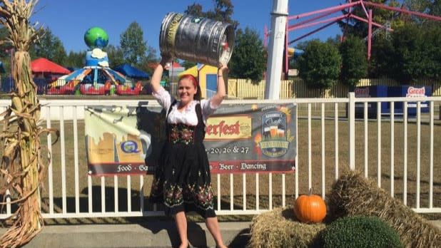 A girl dressed in Oktoberfest clothing holds a keg above her head at Six Flags Great Escape