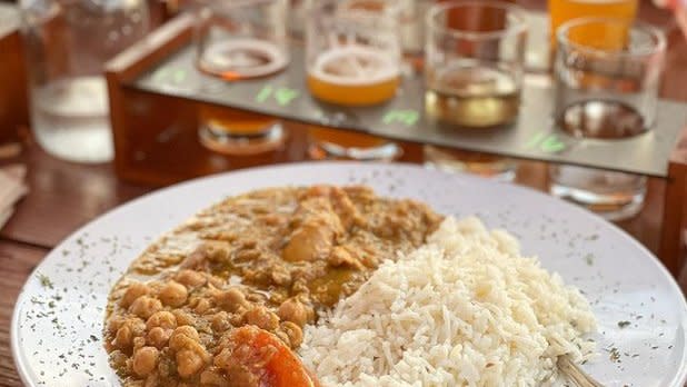 A bowl of chicken curry and white rice with a flight of beers in the background at Hunter Mountain Brewery